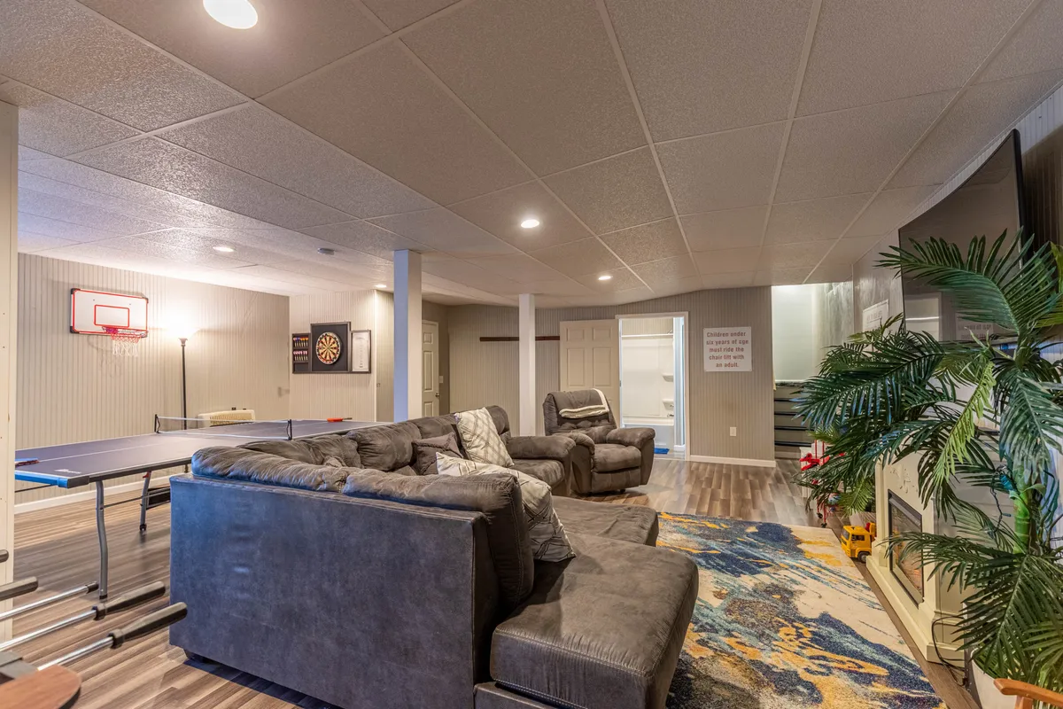 This image captures a lively game room featuring a central ping pong table, a dartboard mounted on the wall, and a comfortable sofa seating area adjacent to a cozy fireplace. The arrangement invites both competitive gameplay and relaxed socializing.