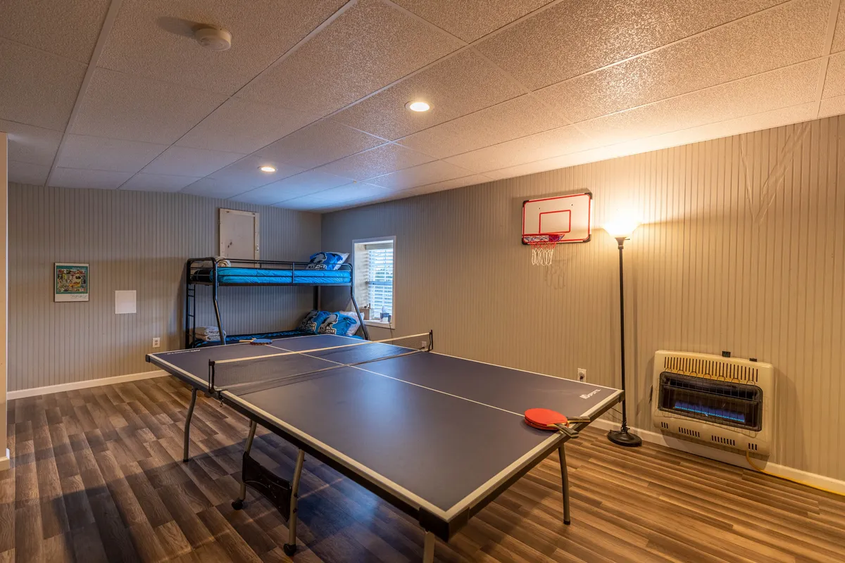 A vibrant game room featuring a ping pong table, bunk bed, basketball hoop, and a lamp. The space is energetic, designed for fun sleepovers, games, and accommodating multiple guests or children.