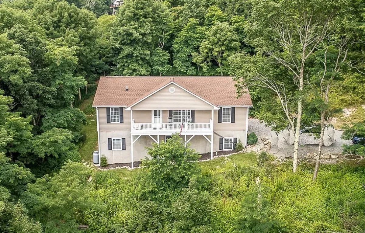 The house's exterior is nestled amidst lush greenery, with a cozy front porch and a well-maintained yard. The inviting atmosphere hints at opportunities for morning coffee, exploring the woods, and relaxing with family or pets in the natural surroundings.