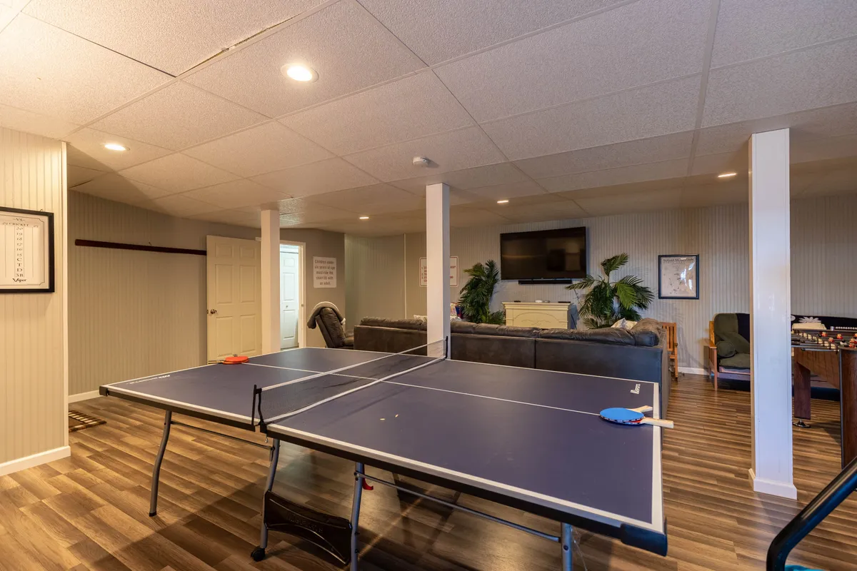 The scene spotlights a ping pong table set up in a recreational area with a plush sofa, a large TV mounted on the wall, and space for family gatherings or movie nights.