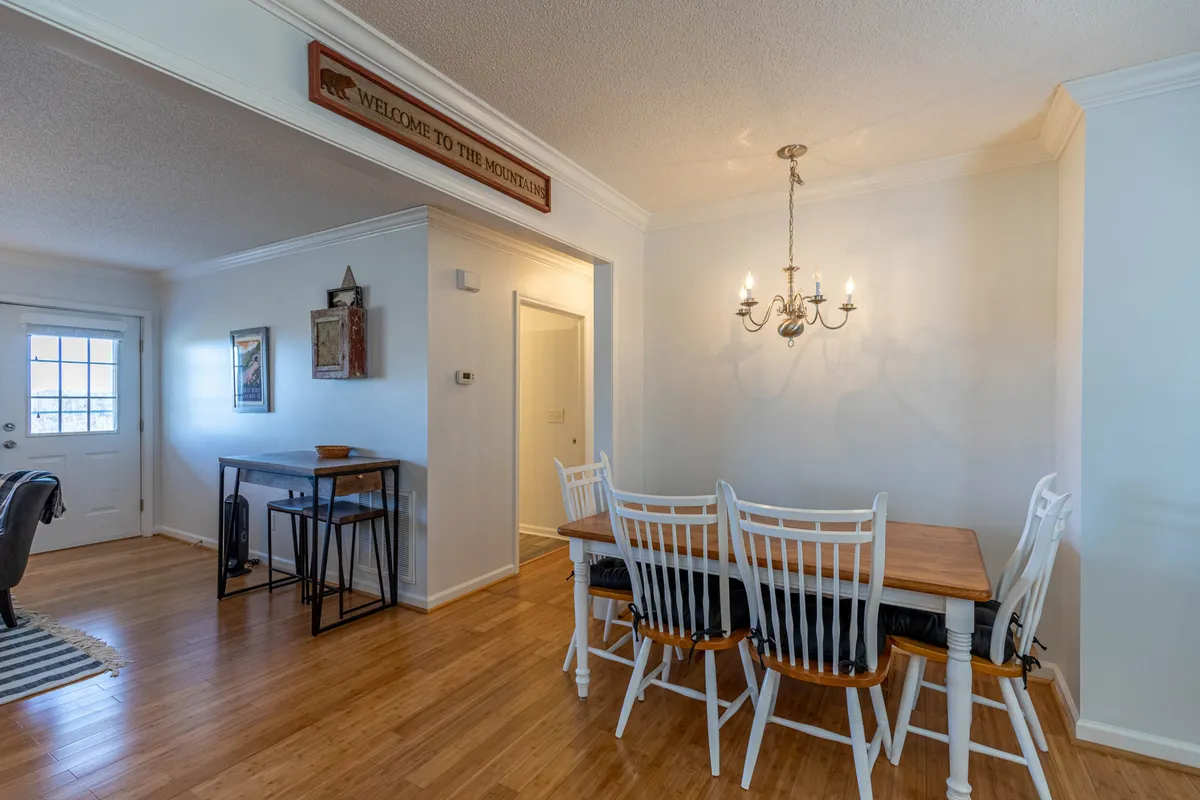 A warm dining space centered around a wooden table with a chandelier above, flanked by welcoming décor and a 'welcome' sign. The setting is bathed in soft natural light, creating an inviting spot for family meals and celebrations.