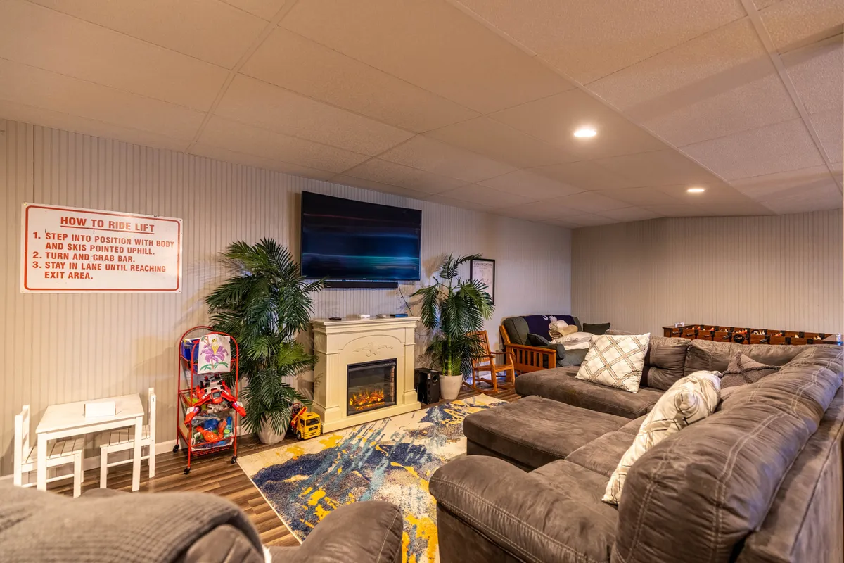 A large sectional sofa, a glowing fireplace, a big-screen TV, and an arcade game are visible in this inviting game room. The space exudes comfort and entertainment, with plenty of seating for family gatherings and activity options that include movies and games.